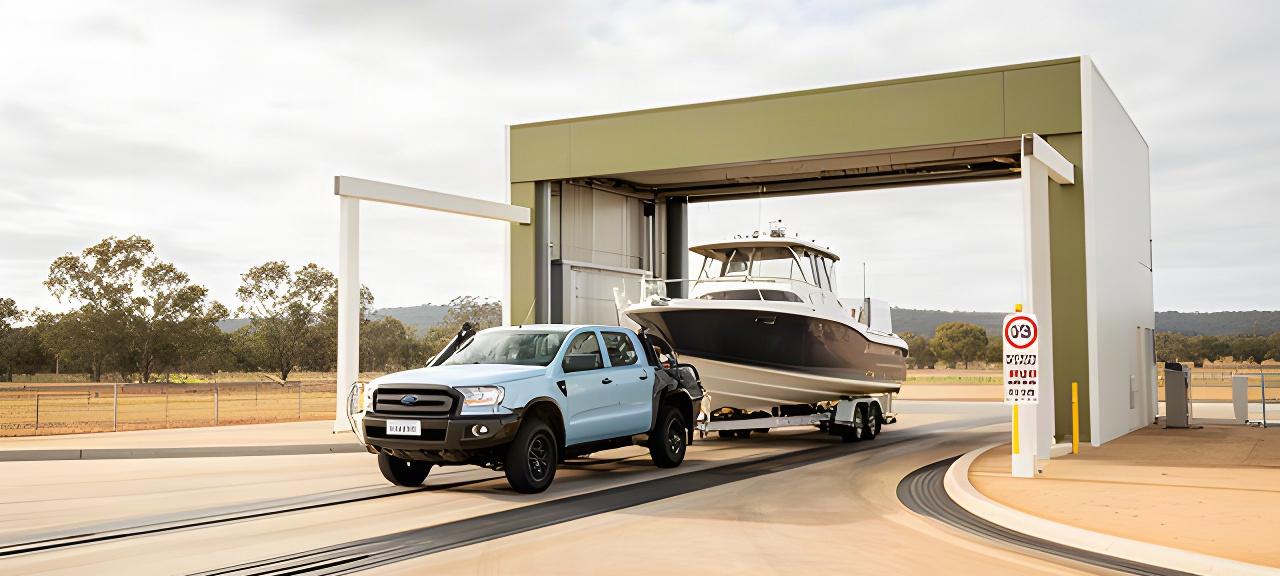 A light commercial truck and boat trailer approaching a spacious high-clearance wash bay